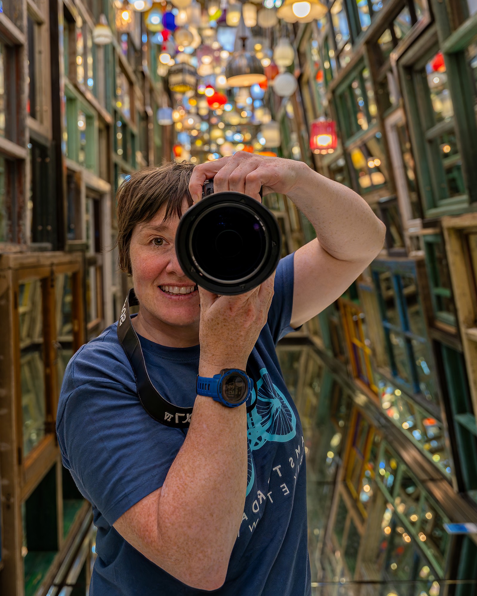 Jane Hasselmann mit der Kamera am Auge, gespiegelt in einer Passage aus alten Fensterrahmen